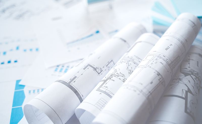 Rouleaux de plans d'architecte grand format posés sur une table de travail